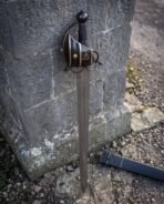 Bars of the blackened cage guard curving over the grip, each one banded with polished brass