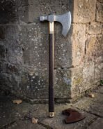 Bearded axe with etched knotwork head, brass collar and Valknut butt cap leaning on a stone corner beside a brown leather mask