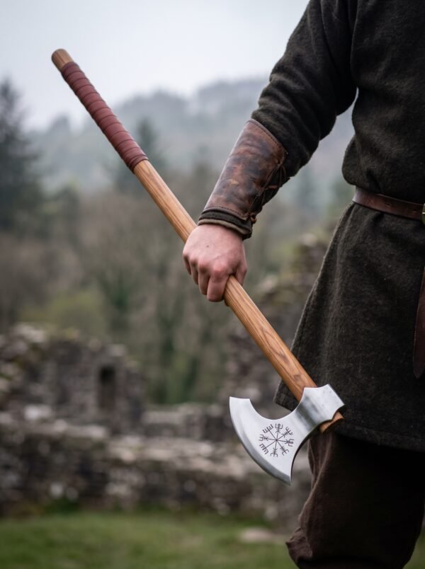 Bearded Viking axe with Vegvisir engraved head and long hardwood haft carried in one hand near ruined stone walls