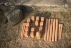 Beech kubb lawn game set laid out on dry grass with king, blocks, throwing batons and corner pins beside an olive canvas bag