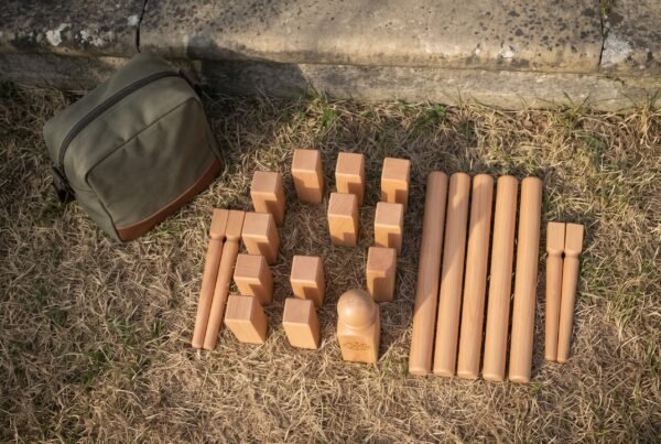Beech kubb lawn game set laid out on dry grass with king, blocks, throwing batons and corner pins beside an olive canvas bag