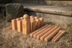 Beech kubb set stacked on grass with the round topped king, ten blocks and six batons in front of a green canvas carry bag