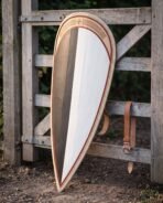 Black and white kite shield with rawhide rim and red trim leaning on a gate, leather strap hanging on the rail
