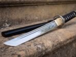 Black cord wrapped over pale ray skin in diamond turns, finished with a round brass tsuba and kashira