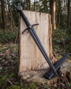 Black knight sword leaning across a mossy tree stump, the faceted pommel showing its engraved Yggdrasil tree panel above a cord wrapped grip and blackened blade