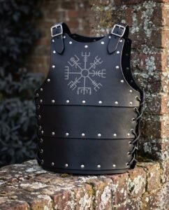 Black leather cuirass with an engraved Vegvisir sigil, domed steel studs and laced side flanks, standing on a weathered brick wall in cold winter light.