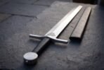 Black leather grip and flat steel disc pommel, black leather scabbard fitted to the blade