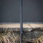 Blackened arming sword with a downswept steel crossguard, Norse knotwork etching and a faceted pommel standing upright against a grey stone kerb