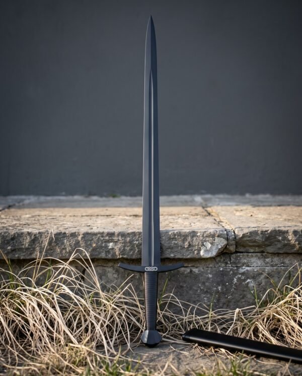 Blackened arming sword with a downswept steel crossguard, Norse knotwork etching and a faceted pommel standing upright against a grey stone kerb