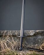 Blackened arming sword with a fullered blade and wire wrapped grip leaning on a low stone wall in dry grass