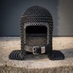 Blackened chainmail armor coif in butted mild steel mail with an integral ventail face flap, bright ring face course and raven stamped leather strap on a stone ledge