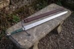 Blackened crossguard with scrolled arms and clover shaped terminals above a green leather grip