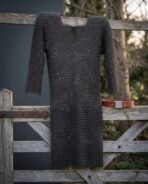 Blackened mild steel chainmail hauberk hanging from a wooden field gate, knee length with a split neck, red leather belt resting on the rail