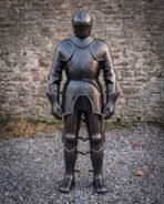 Blackened plate armour suit standing straight on with closed helm, fluted breastplate and rune line on a gravel yard