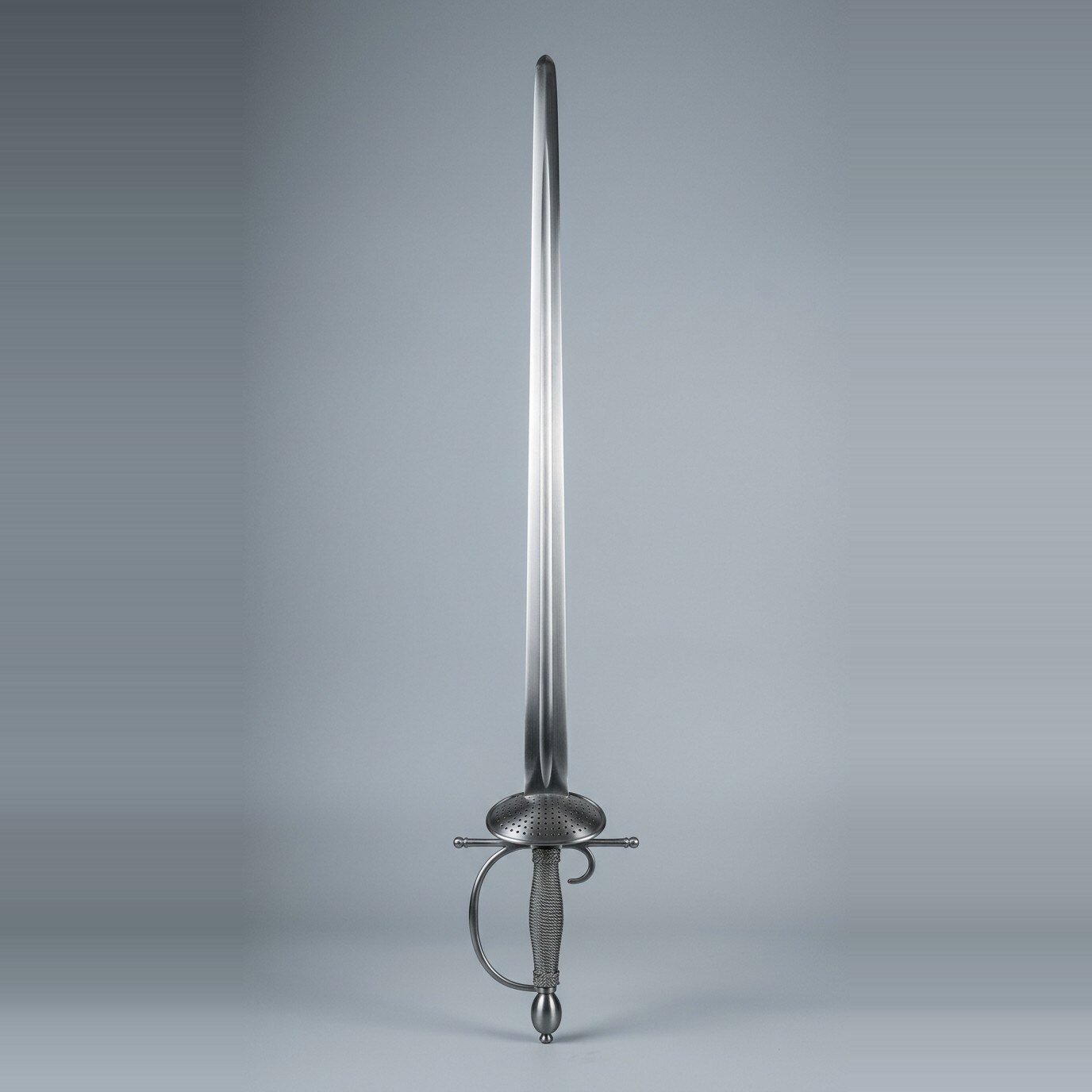 Hrafnstede Blackened Smallsword Trainer RK-3010 Blackened smallsword trainer with a pierced oval shell guard, olive pommel and dark wire bound grip standing point up against a plain grey studio backdrop