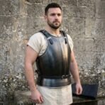 Blackened steel breastplate with chased knotwork on the chest and leather shoulder straps worn over a cream tunic by a dark haired man