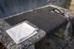 Blackened steel chainmail shirt laid on a stone bench with a folded cream linen cloth and a black leather belt