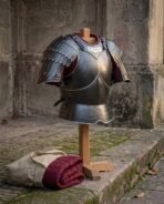 Blackened steel cuirass with scaled pauldrons, hooped fauld, rune plaque and burgundy lining on a wooden stand, angled by a stone wall