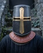 Blackened steel great helm with brass rune cross worn by a man over a chainmail collar and brown leather gorget on mossy stone steps