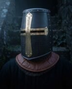 Blackened steel great helm with brass rune lettered cross and riveted brow band worn at an angle over a chainmail collar and tan leather gorget