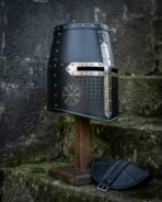 Blackened steel great helm with polished cross reinforce, chased vegvisir and domed rivets on a wooden stand, angled on mossy stone steps