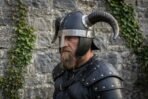 Blackened steel horned helmet with buffalo horns and rune brow band worn by a bearded man in leather armour