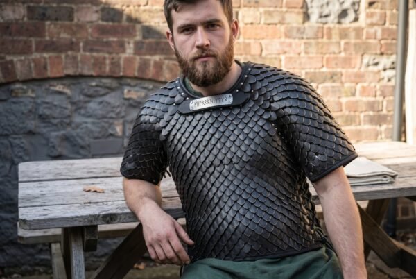 Blackened steel scale armour shirt with a rune plaque at the throat worn by a bearded man seated at a garden table