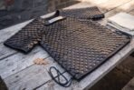 Blackened steel scale armour shirt with short sleeves laid flat on a weathered wooden table with oak leaves and side laces