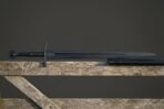 Blackened valknut sword with a dark fullered blade, a black corded grip and a round pommel, resting on a weathered timber fence rail against a grey sky