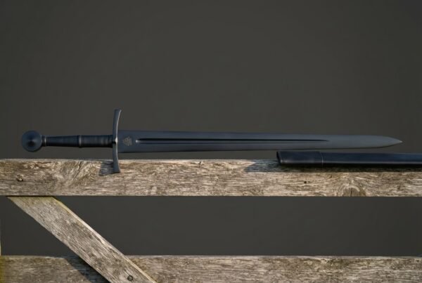 Blackened valknut sword with a dark fullered blade, a black corded grip and a round pommel, resting on a weathered timber fence rail against a grey sky