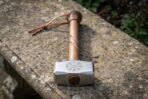 Blacksmith hammer with Vegvisir engraved head and carved spiral wooden handle with leather thong resting on a stone wall