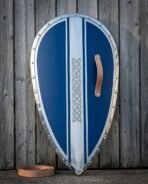 Blue and polished steel Norman kite shield with a riveted rim, Celtic knotwork centre band and tan leather grip standing against a weathered grey wooden fence