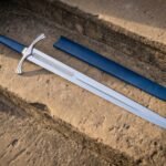 Blue leather longsword with a polished steel blade, brass fluted pommel and curved crossguard resting beside its scabbard on sunlit sandstone steps