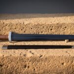 Blued viking sword with a lobed pommel and tan leather grip lying beside its black leather scabbard on a warm sandstone ledge in low evening light