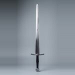 Blunt longsword for sparring with a fuller to mid blade, wheel pommel and black leather grip standing point up against a plain grey studio backdrop