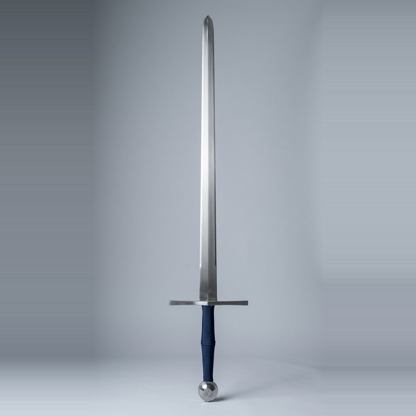 Drakvend blunt longsword trainer RK-3004 Blunt longsword trainer with a flat diamond section double edged blade, wheel pommel with a raised boss and navy cord wrapped two hand grip on a plain studio backdrop