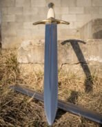 Close up of the brass bell pommel, ribbed bone toned grip and downswept guard on a steel sword leaning on a stone block
