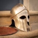 Brass Corinthian Greek helmet with engraved meander brow band seen in three quarter view on a sandstone step
