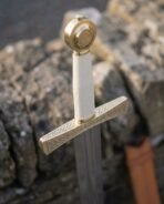 Brass hilt arming sword with wheel pommel, ivory toned grip and Celtic knotwork cross guard against grey stone