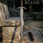 Brass hilt damascus sword standing point down in a walled garden showing feather pattern steel, rune cut brass guard and oxblood leather grip and scabbard