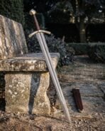 Brass hilt Damascus sword with dark leather grip leaning on a garden stone bench with its brass tipped scabbard on the paving