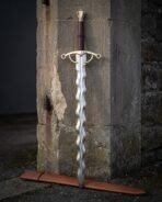 Brass hilt flamberge sword with a wavy flame blade in satin 1095 steel, ring terminal guard and faceted brass pommel standing against an old stone doorway