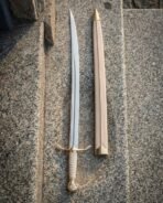 Brass hilted sabre with a pale wrapped grip and rosette pommel laid on granite next to its pale leather scabbard