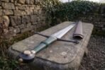 Bright polished arming sword blade carrying three narrow parallel fullers and a framed Celtic interlace band