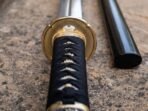 Bright single edged tanto against warm brass furniture, supplied with a fitted matt black scabbard