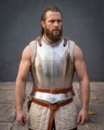 Bright steel breastplate with chased knotwork and rune lettering on the chest, worn over a quilted tunic by a bearded man with braided hair
