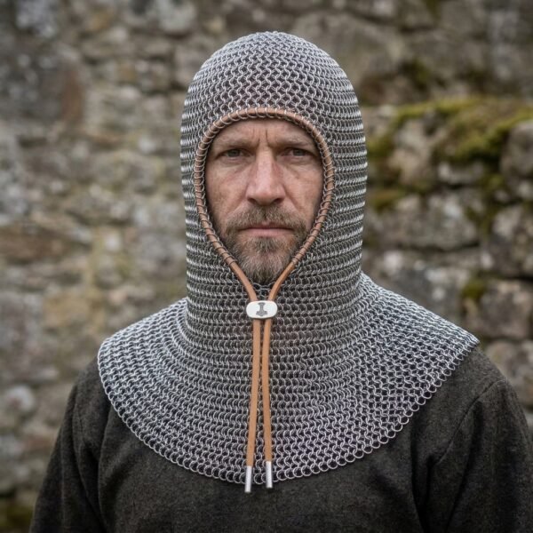 Bright steel chainmail coif with leather edged face opening and tan drawstring throat worn by a bearded man against a mossy stone wall