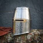 Bright steel great helm with brass cross reinforce, knotwork etched sights and domed brass rivets, angled on a mossy brick wall
