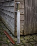 Broad Damascus blade with a long central fuller under an arched blackened guard edged in brass