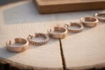 Bronze tone open cuff rings, plain valknut stamped bands and twisted wire bands standing in a row on a sawn log